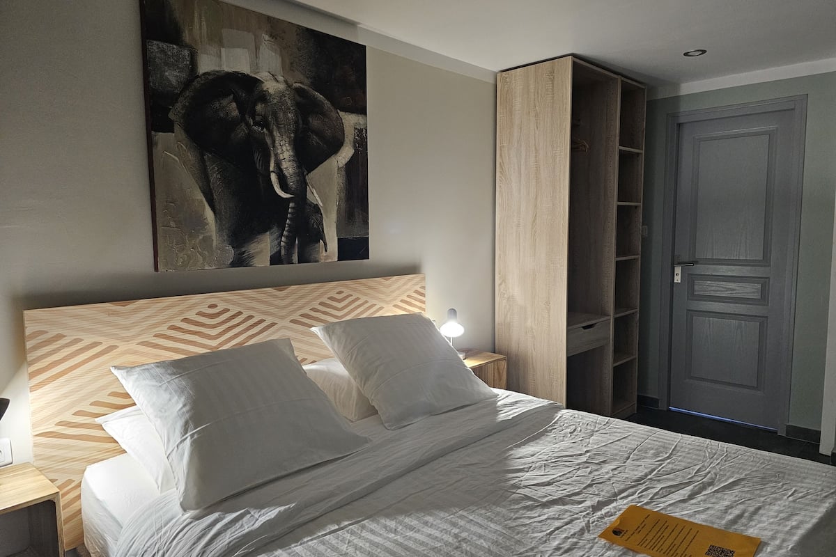 Een hotelkamer met een bed, een nachtkastje, een kunstwerk van een olifant aan de muur, een kledingkast en een deur.