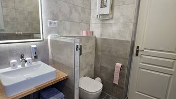 Un baño moderno con un espejo grande, un lavabo, un inodoro y una zona de ducha.
