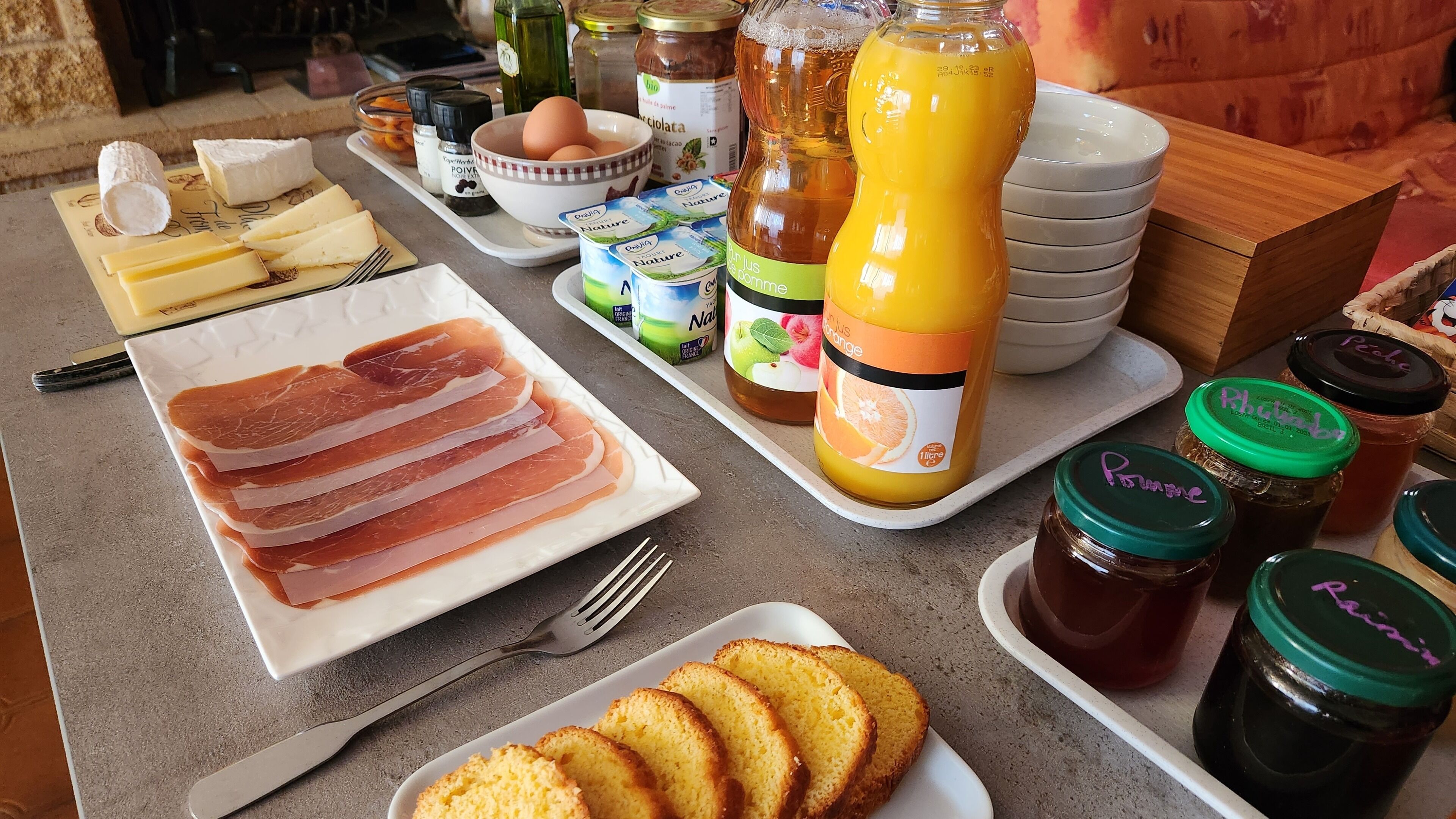Una mesa de desayuno con diversos alimentos, incluyendo queso, jamón, huevos, jugo y salsas.
