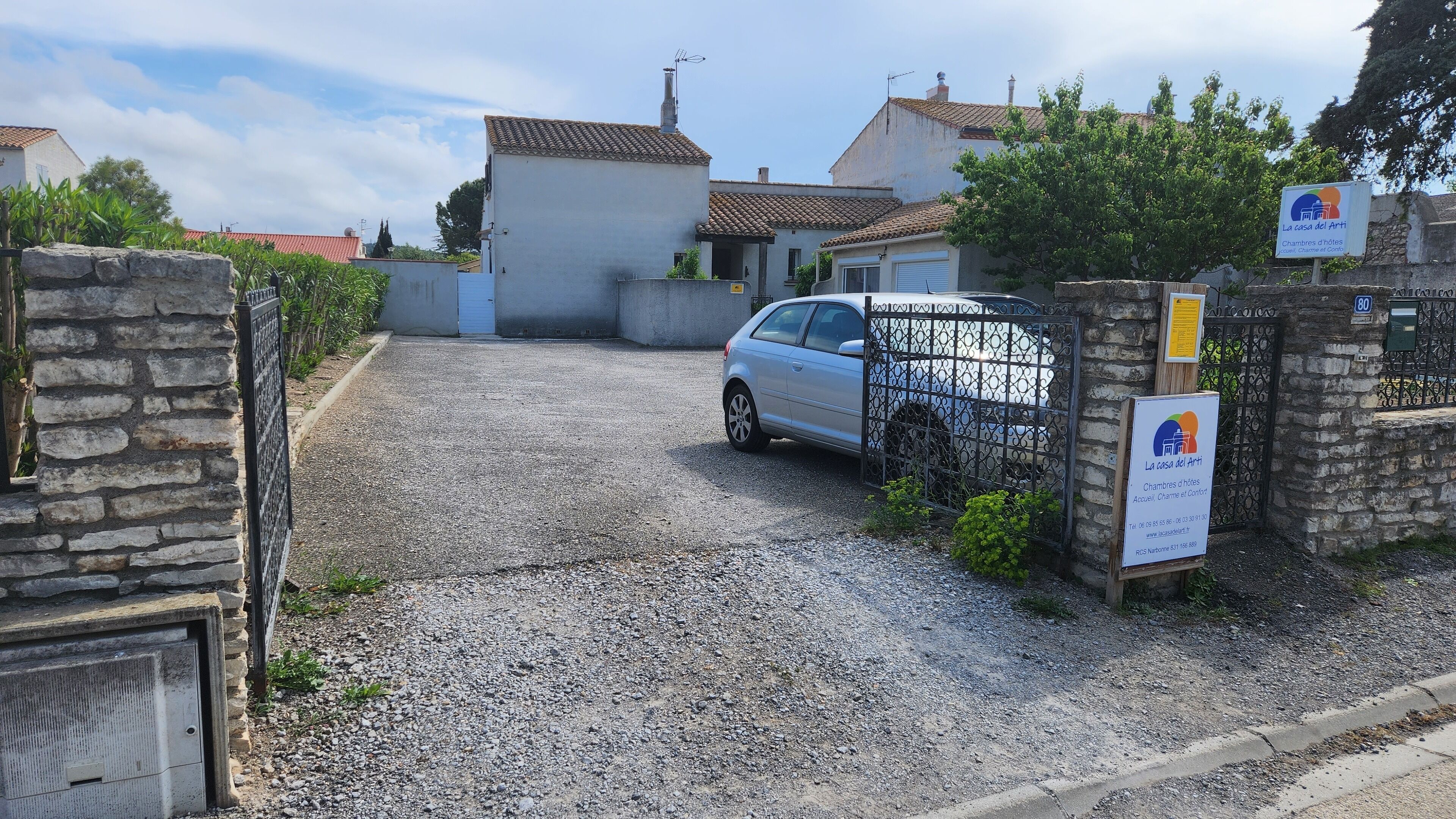 Un camino de grava que conduce a una entrada con puerta y un coche estacionado.