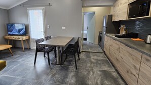 Een moderne keuken met een inbouwmagnetron, oven en spoelbak. Er is een eethoek met een tafel en stoelen, en een televisie op een standaard.
