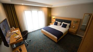 Habitación de hotel con cama, escritorio con silla, televisor y ventana con cortinas.