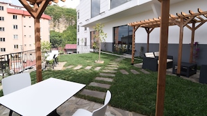 Un patio exterior moderno con pérgola, asientos y un árbol pequeño.