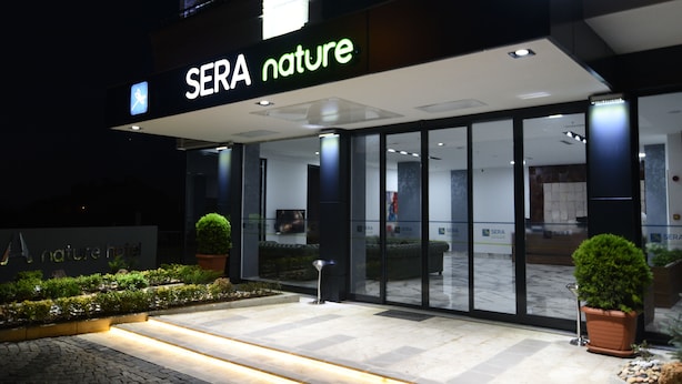 Entrada de un hotel con un letrero que dice "SERA nature" y un sendero bien iluminado que lleva a la entrada.