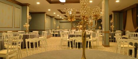 Una sala da banchetto con tavoli rotondi, sedie bianche e lampadari decorati.