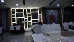 Un comedor moderno con mesas y sillas, una pared con paneles iluminados, y un ventanal grande.