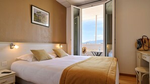 A hotel room with a large bed, a bedside table, a chair, a desk, and a view of the outdoors. - Hotel du Golfe (Ajaccio)