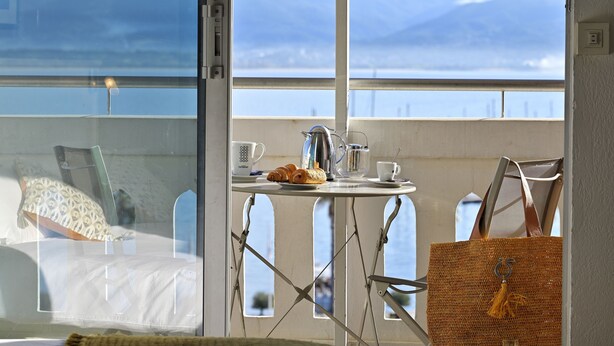 A balcony with a table set for breakfast, a chair, and a view of the sea and mountains. - Hotel du Golfe (Ajaccio)