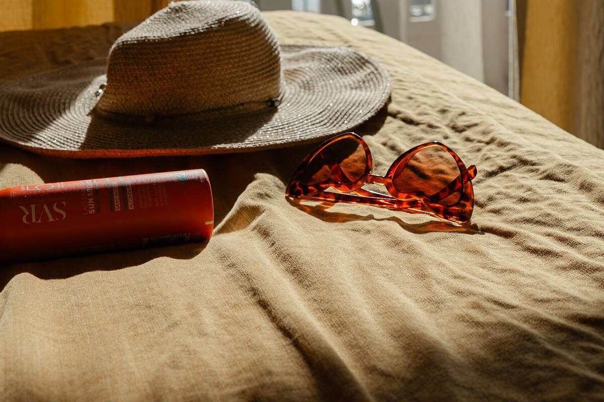 A bed with a straw hat, sunglasses, and a book on a textured bedspread.