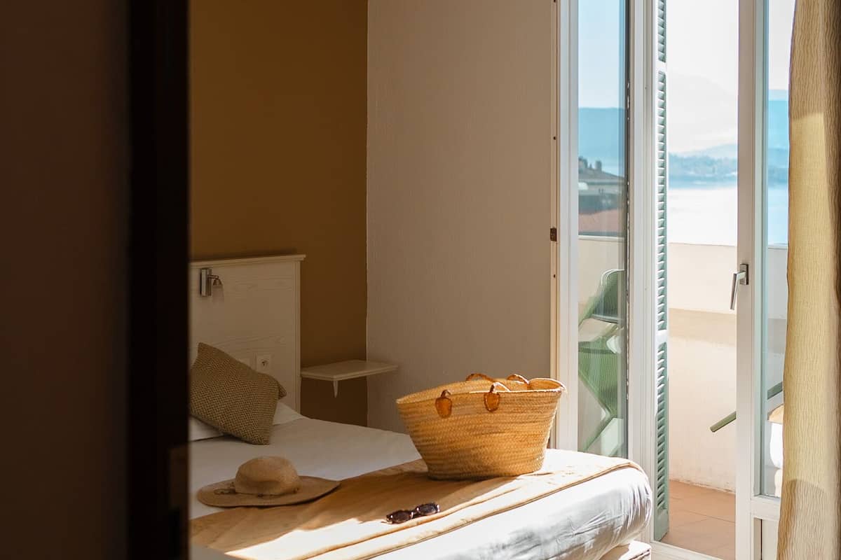 A bedroom with a bed, a bedside table, a basket, and a view of the outdoors through a sliding door.