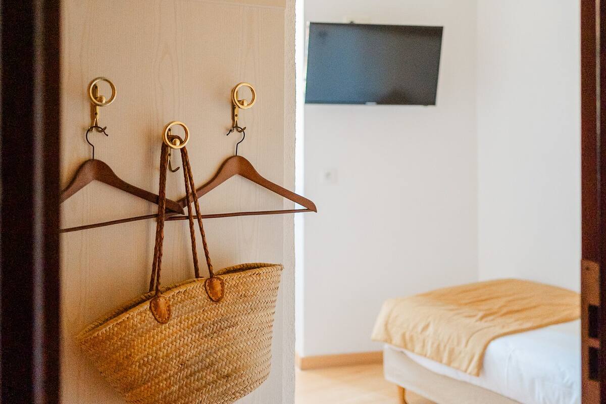 A room with a bed, a wall-mounted TV, and a hanging basket with a bag.