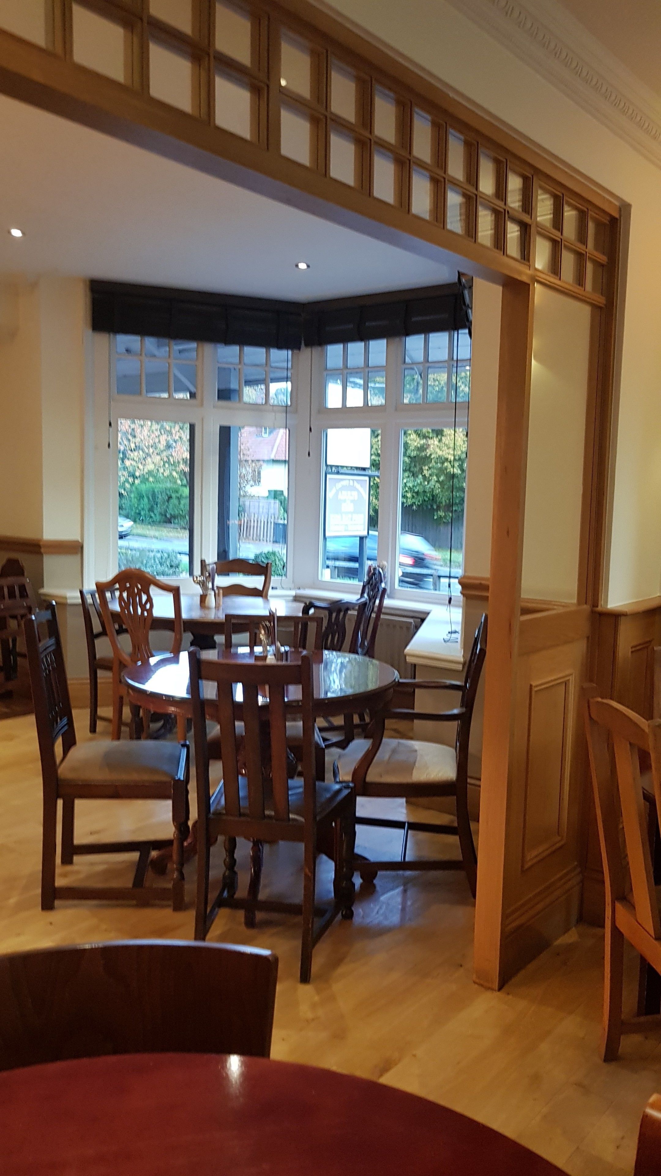 A dining area with wooden furniture, large windows, and a view of the street outside.