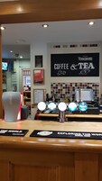 A coffee and tea shop interior with a counter displaying various drink options, a sign for 'Yorkshire Coffee & Tea', and a Coca-Cola branded cooler.