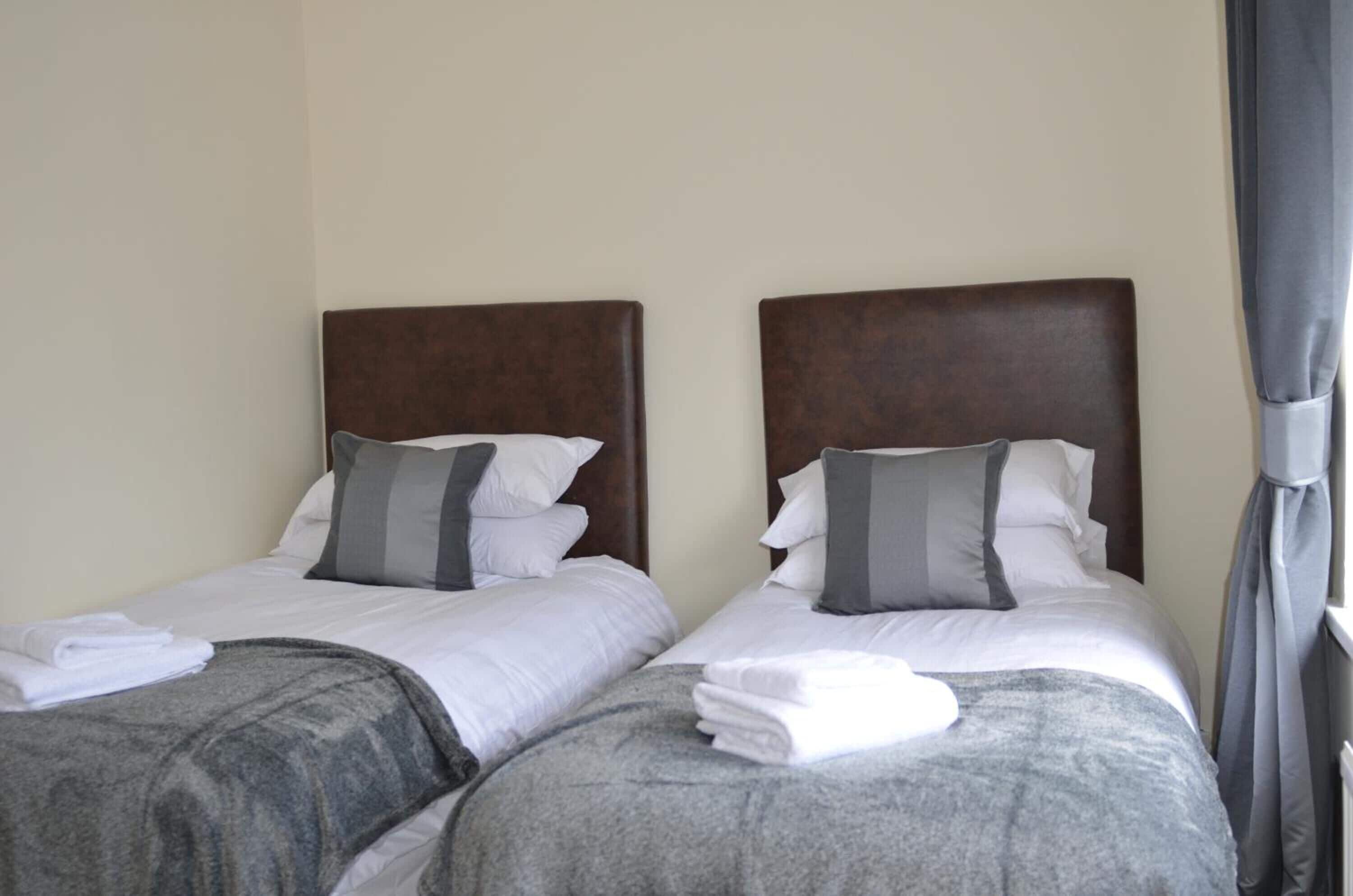 Two single beds with wooden headboards, white bedding, and grey throw blankets.