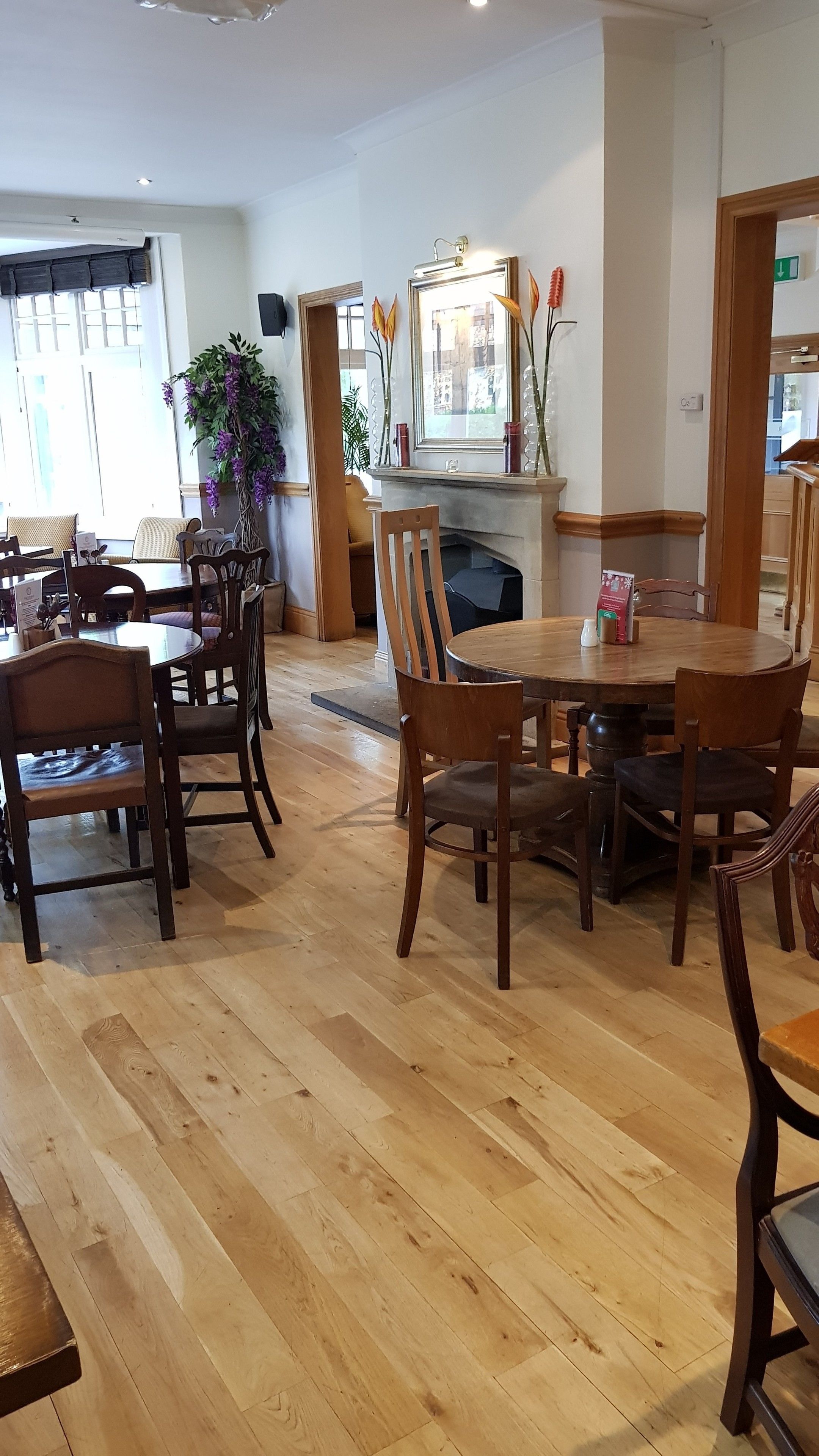 A spacious dining area with wooden tables and chairs, a fireplace, and a large window with a view of the city.