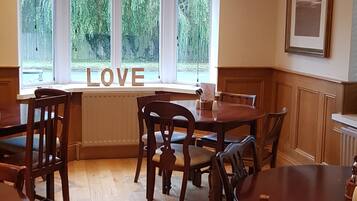 Un comedor con mesas y sillas de madera, un amplio ventanal con vistas a zonas verdes, y la palabra "LOVE" mostrada en el ventanal.