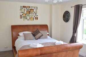 A neatly made bed with a brown headboard, white bedding, and two pillows. A decorative wall piece is above the bed, and a curtain is partially drawn to the side.