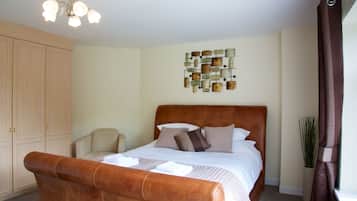 A bedroom with a large bed, a wooden wardrobe, a chair, a decorative wall piece, and a plant.