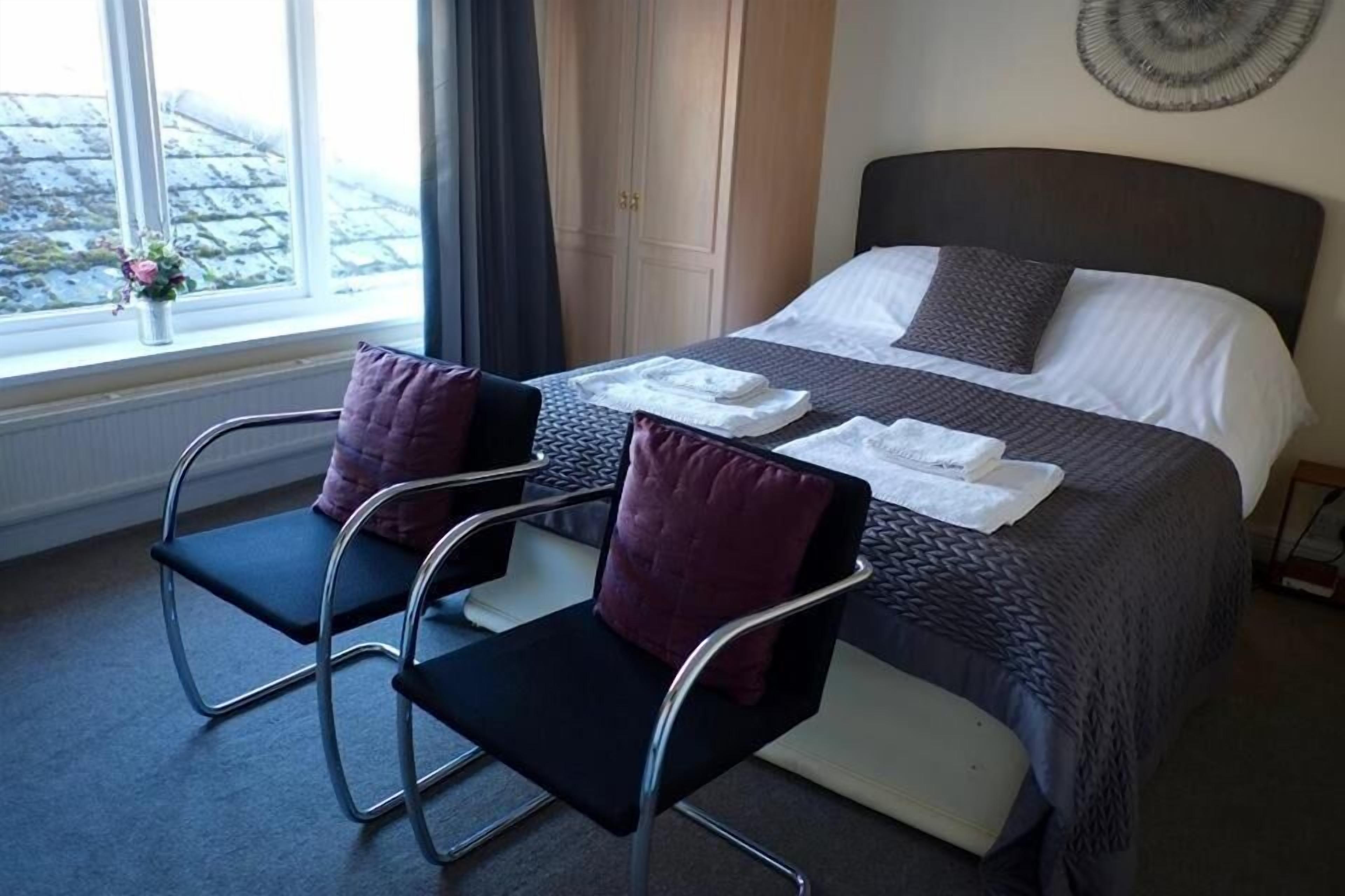 A hotel room with a bed, two chairs, a window with a view, and a door.