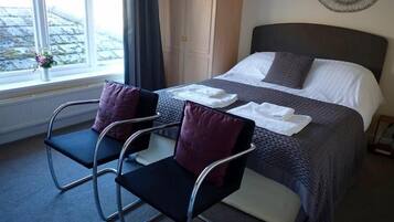A hotel room with a bed, two chairs, a window with a view, and a door.