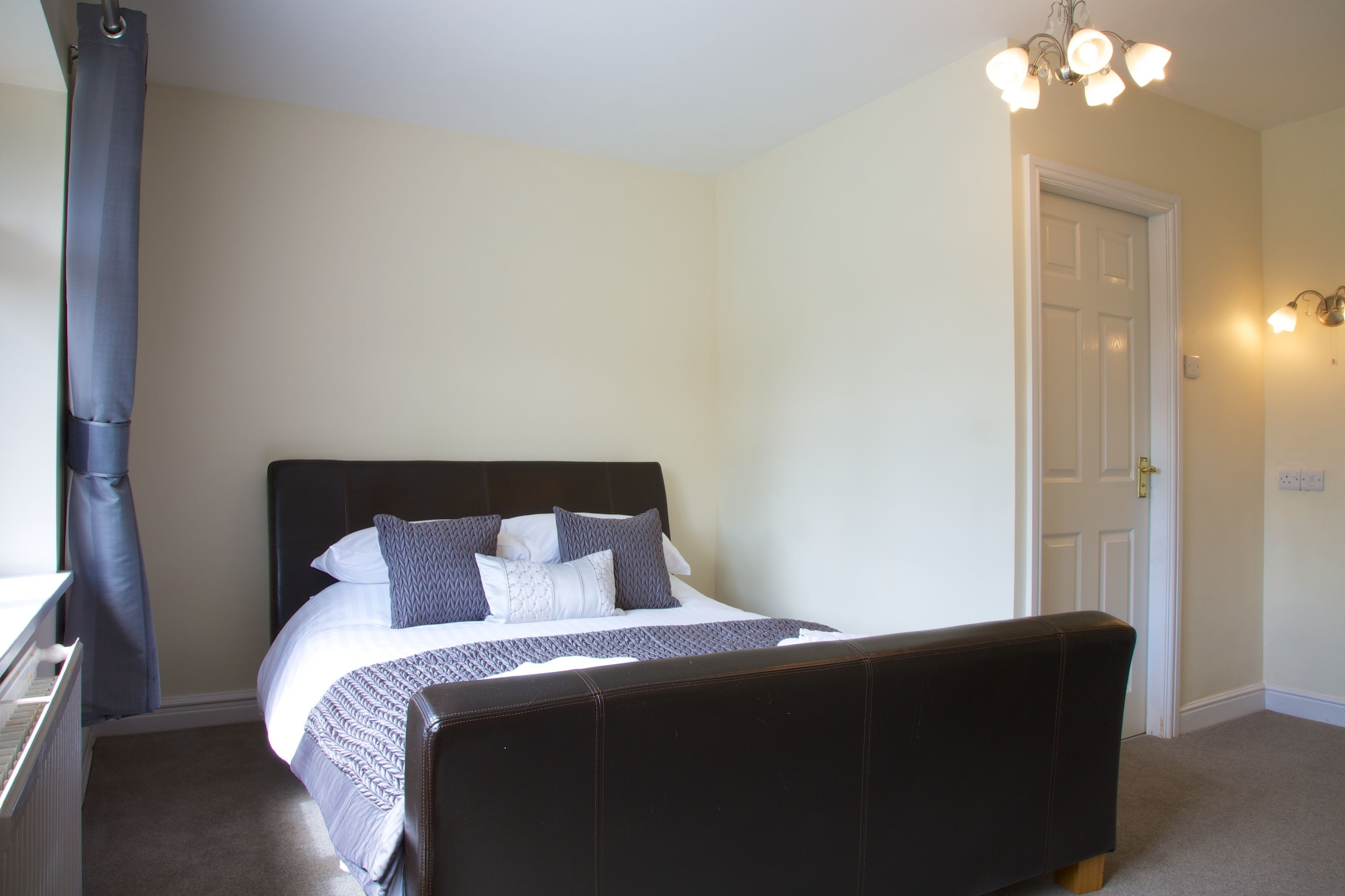 A bedroom with a bed, a bench, a door, and a light fixture.