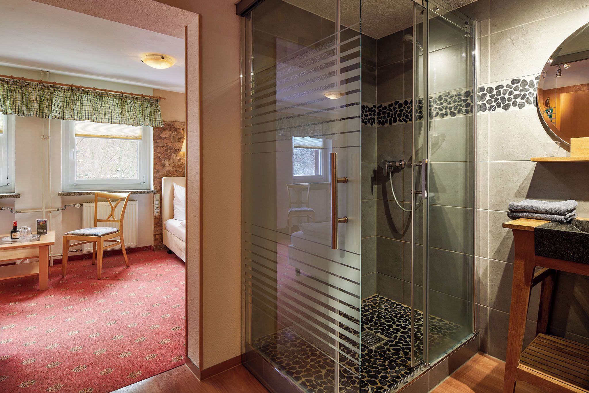 A bathroom with a glass-enclosed shower, a wooden vanity, and a red patterned carpet.
