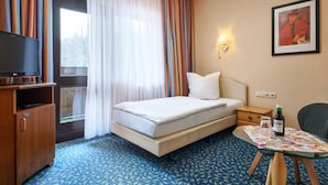 A hotel room with a bed, a TV, a small table with a bottle, and a chair. - Hotel Ladenmühle (Altenberg)
