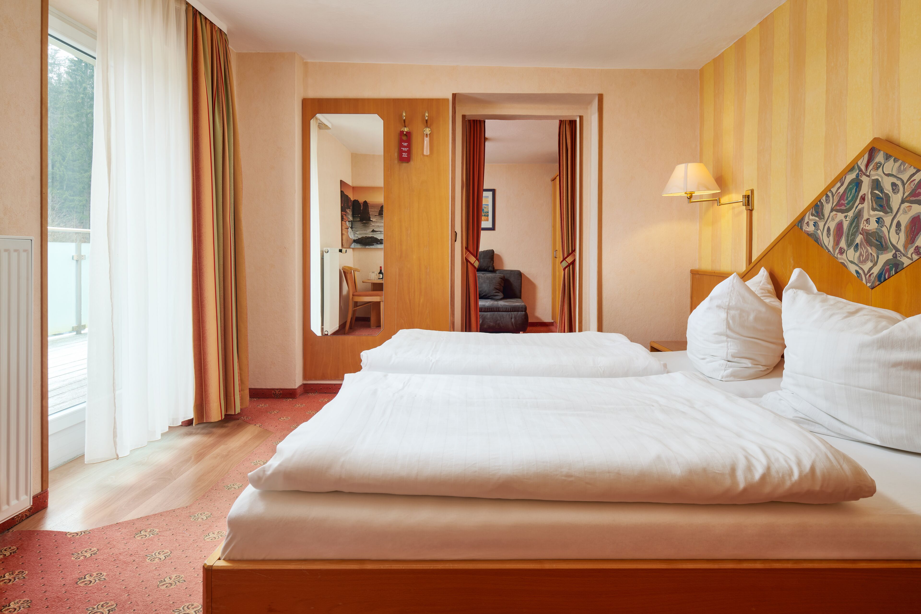 Een hotelkamer met twee bedden, een houten hoofdeinde, een nachtkastje met een lamp en uitzicht op een balkon.