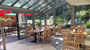 A restaurant with a glass roof, wooden furniture, and a view of the garden. - Hotel Ladenmühle (Altenberg)