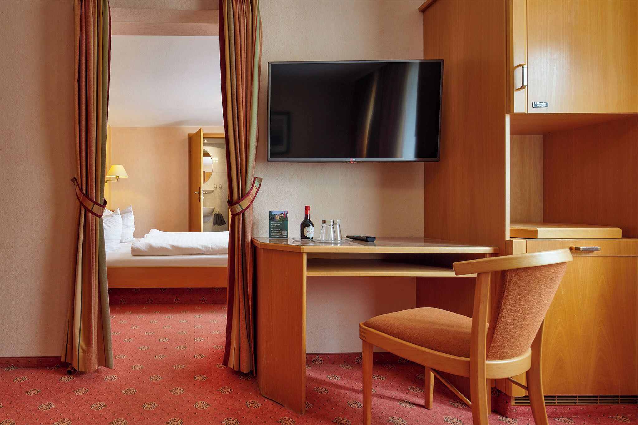 A hotel room with a bed, a desk with a chair, a television, and curtains.