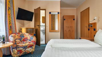 Habitación de hotel con cama, sofá, televisión, baño y puertas de madera.