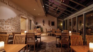 A restaurant with wooden tables and chairs, stone walls, and a glass enclosure. - Hotel Ladenmühle (Altenberg)