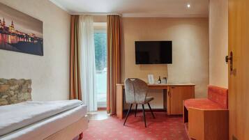 Habitación de hotel con cama, escritorio con silla, televisión y vista a la ciudad a través de una ventana.