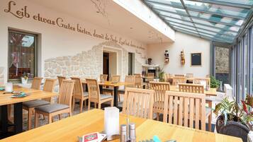 Un restaurant amb taules i caires de fusta, parets de pedra i un sostre de vidre.