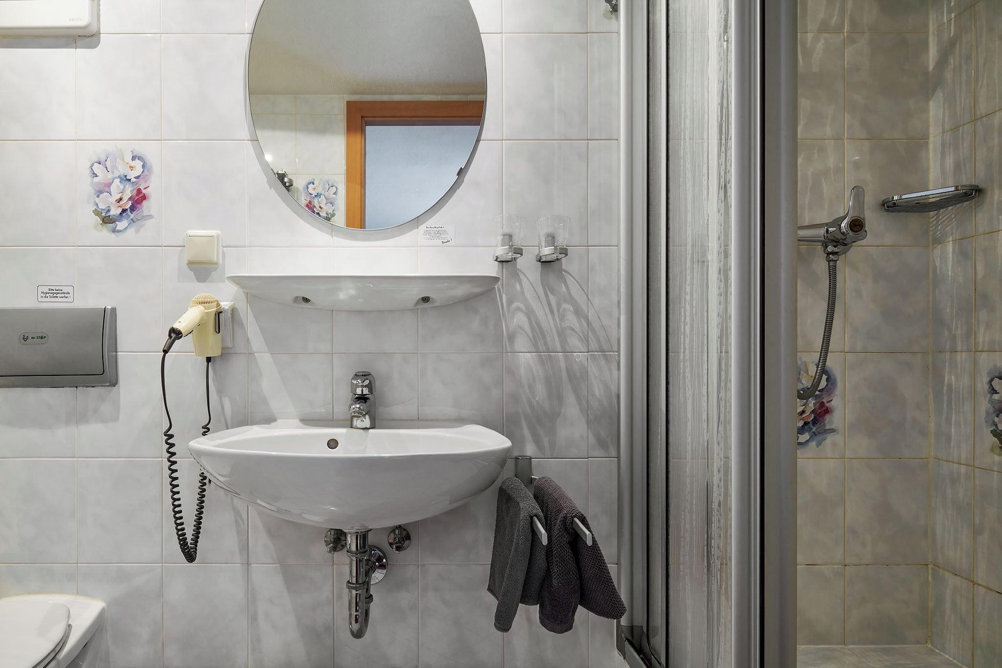A bathroom with a white sink, a mirror, a shower, and a towel rack.