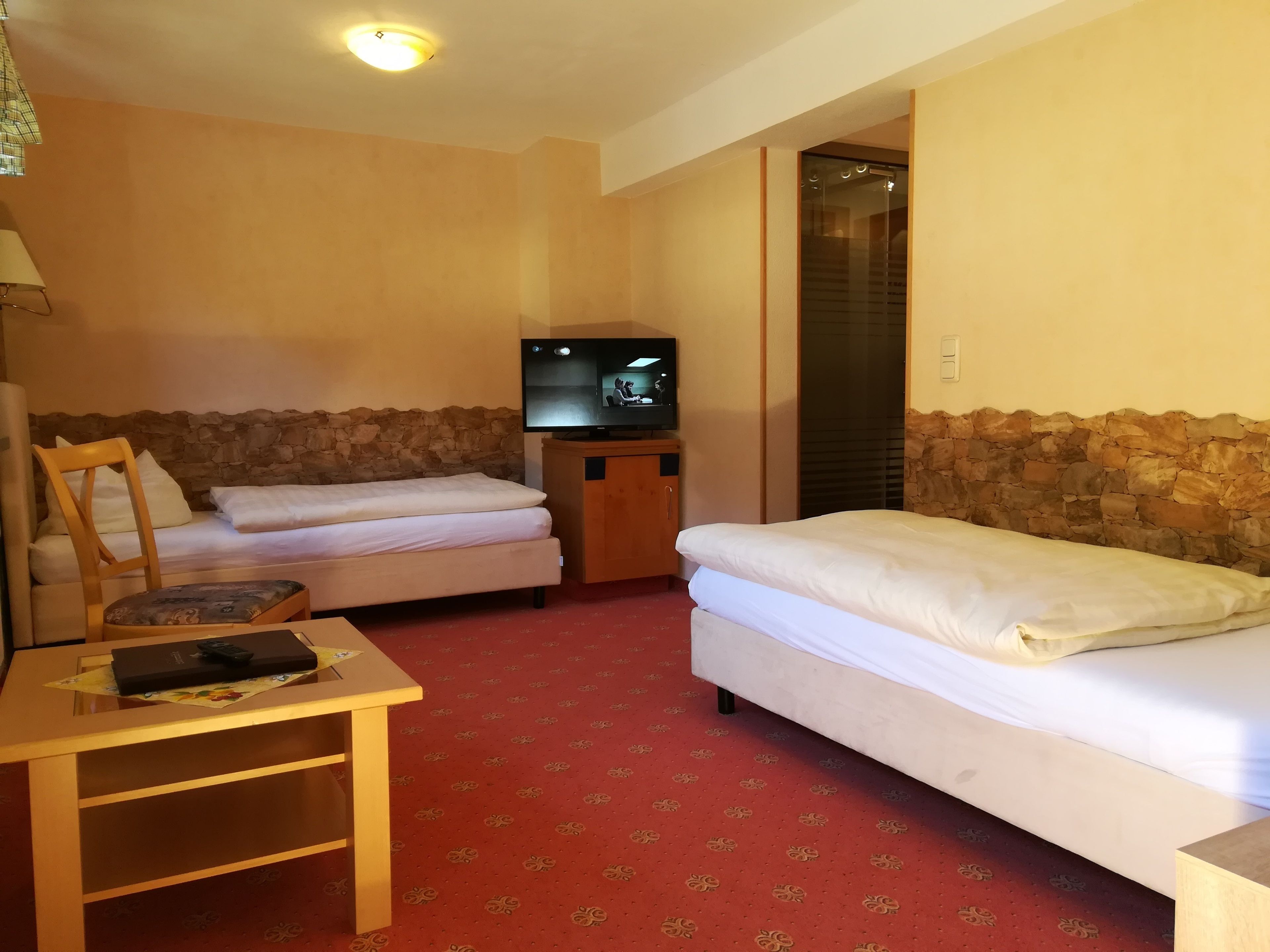Ein Hotelzimmer mit zwei Betten, einem Fernseher, einem Schreibtisch und einer Steinwand.