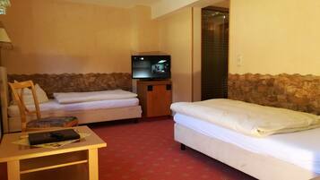 A hotel room with two beds, a TV, a desk, and a stone wall.