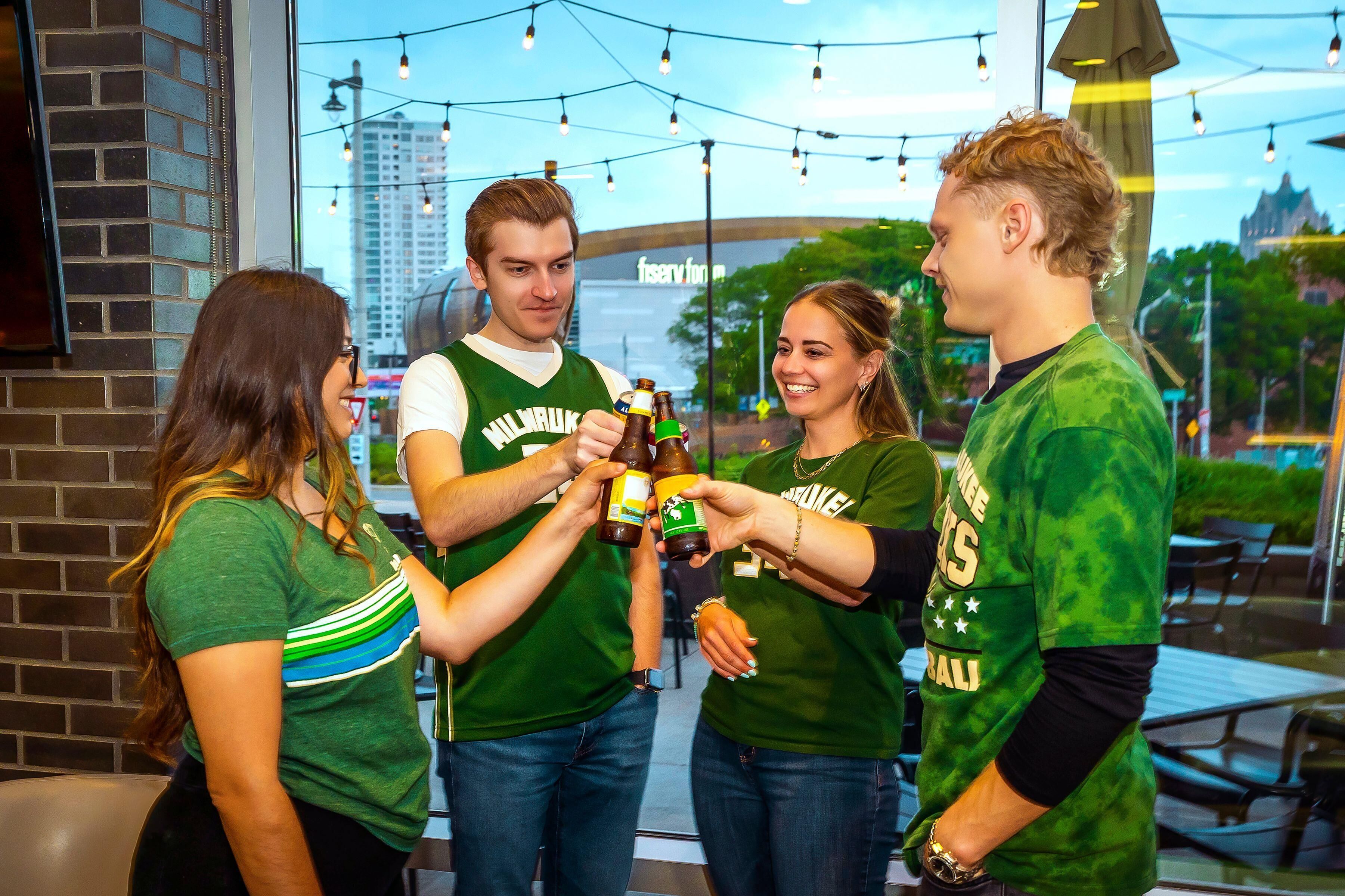 A group of people in a casual setting, possibly a bar or restaurant, with a view of a cityscape through a window.