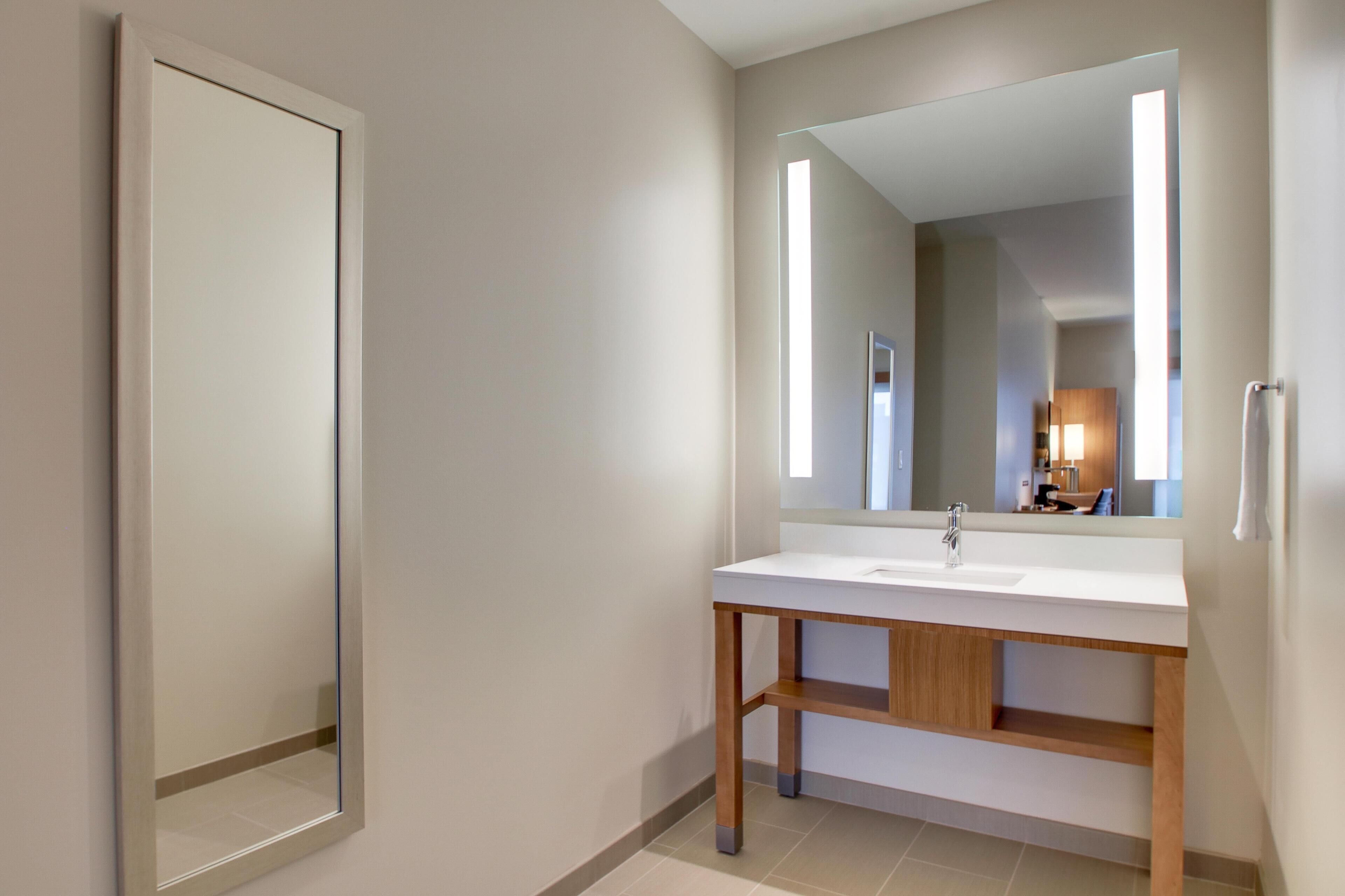 A modern bathroom with a white sink, a large mirror, and a wooden vanity.