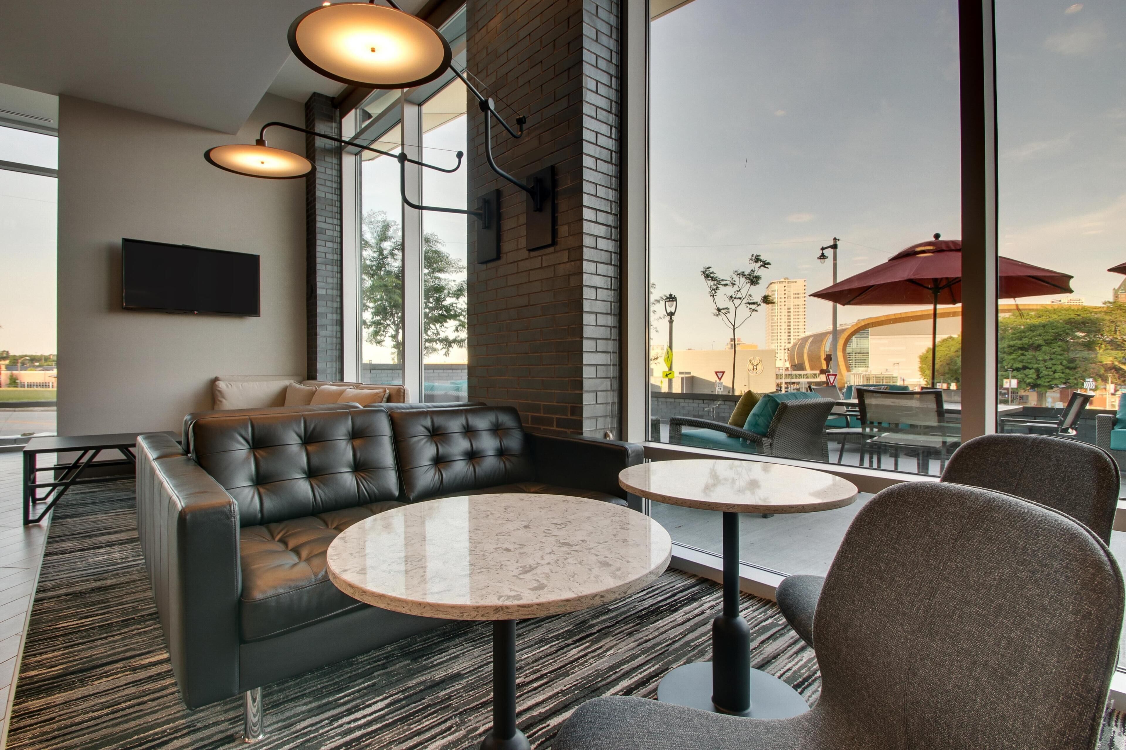 A modern lounge area with a leather sofa, round tables, and large windows offering a view of the cityscape.