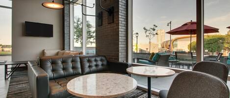 A modern lounge area with a leather sofa, round tables, and large windows offering a view of the cityscape.