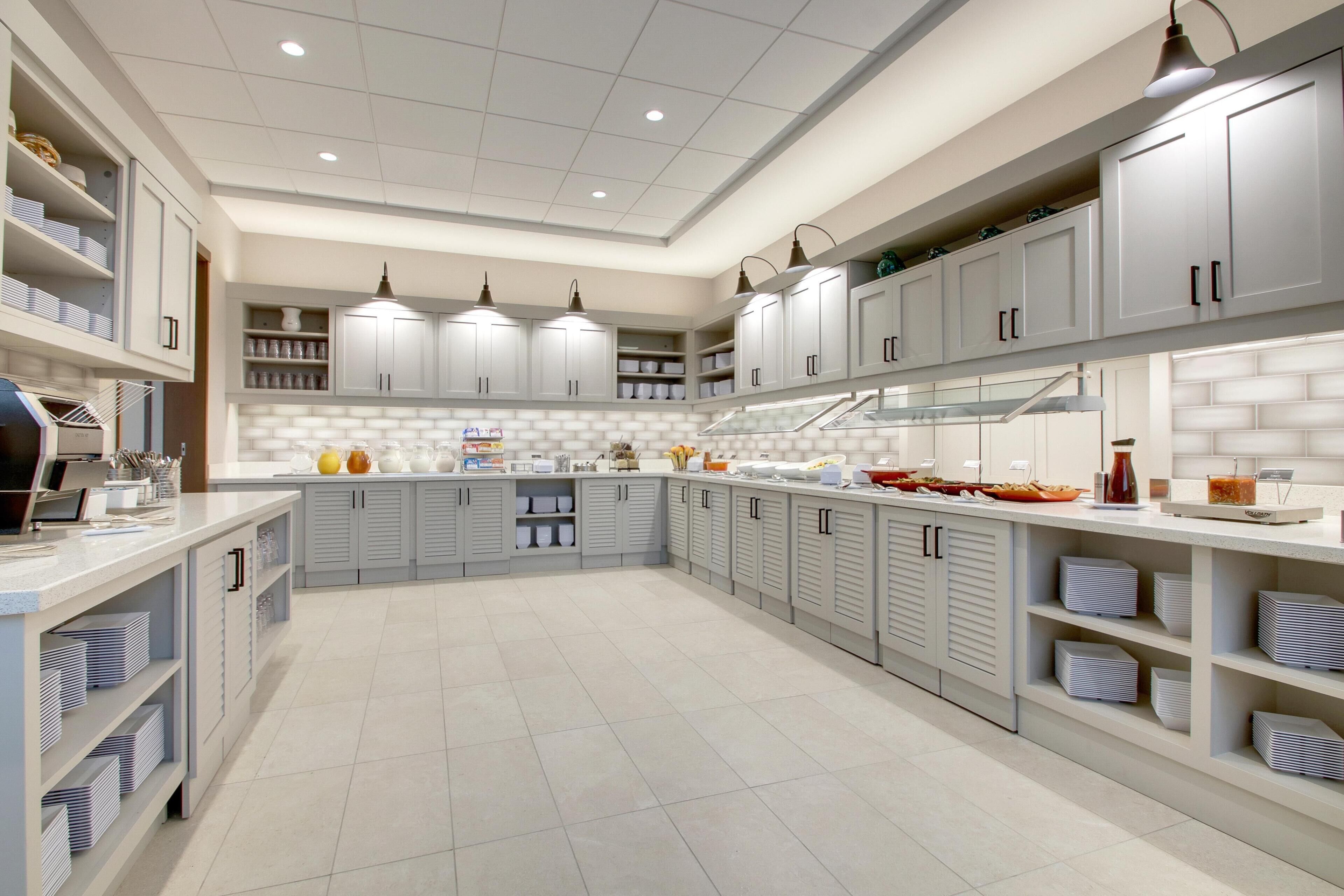 A spacious kitchen with grey cabinets, a central island, and pendant lighting.