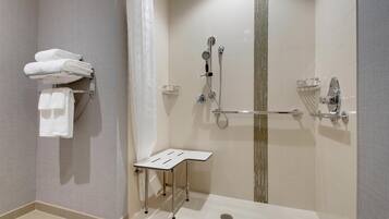 Ett modernt duschutrymme med en dusch som är avskärmad med glasväggar, en handduksställning med hopvikta handdukar och ett litet bord.