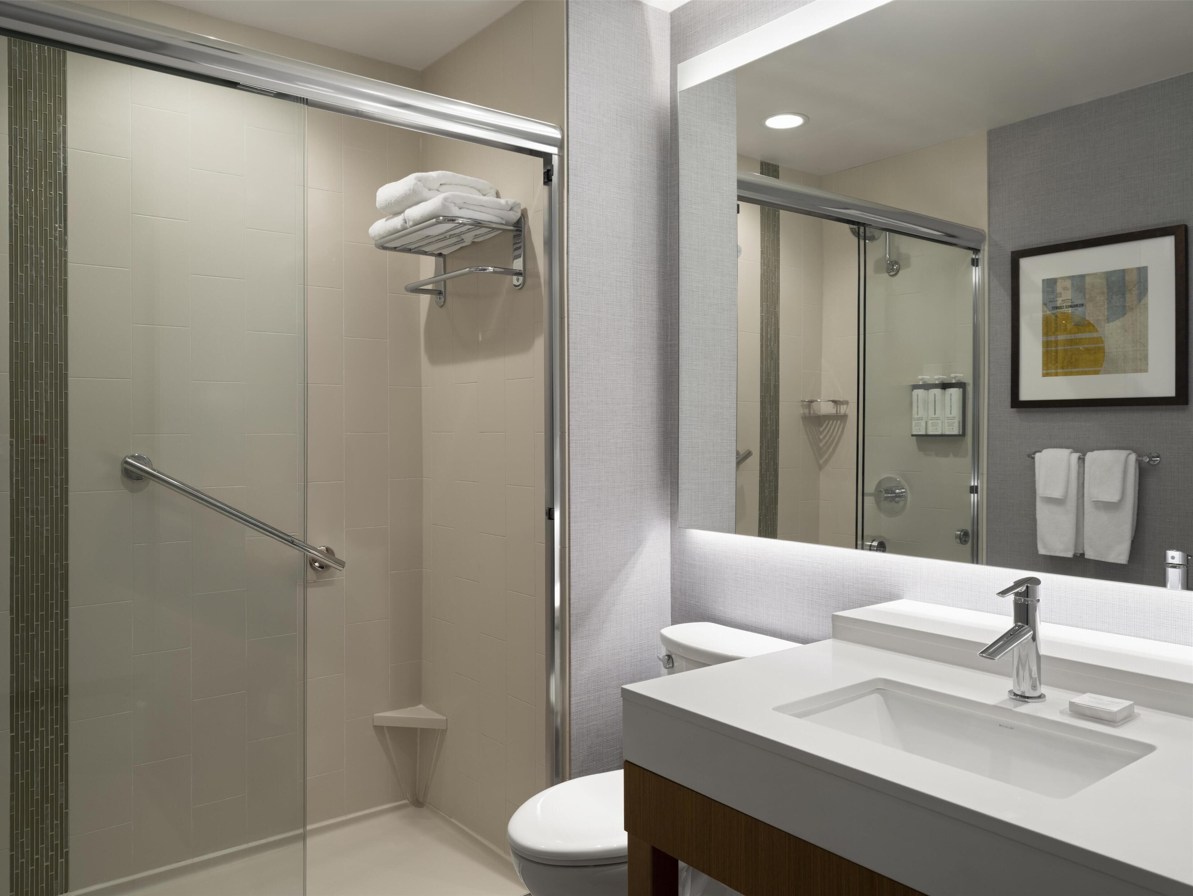 Een moderne badkamer met een douchecabine van glas, een witte wastafel en een toilet.