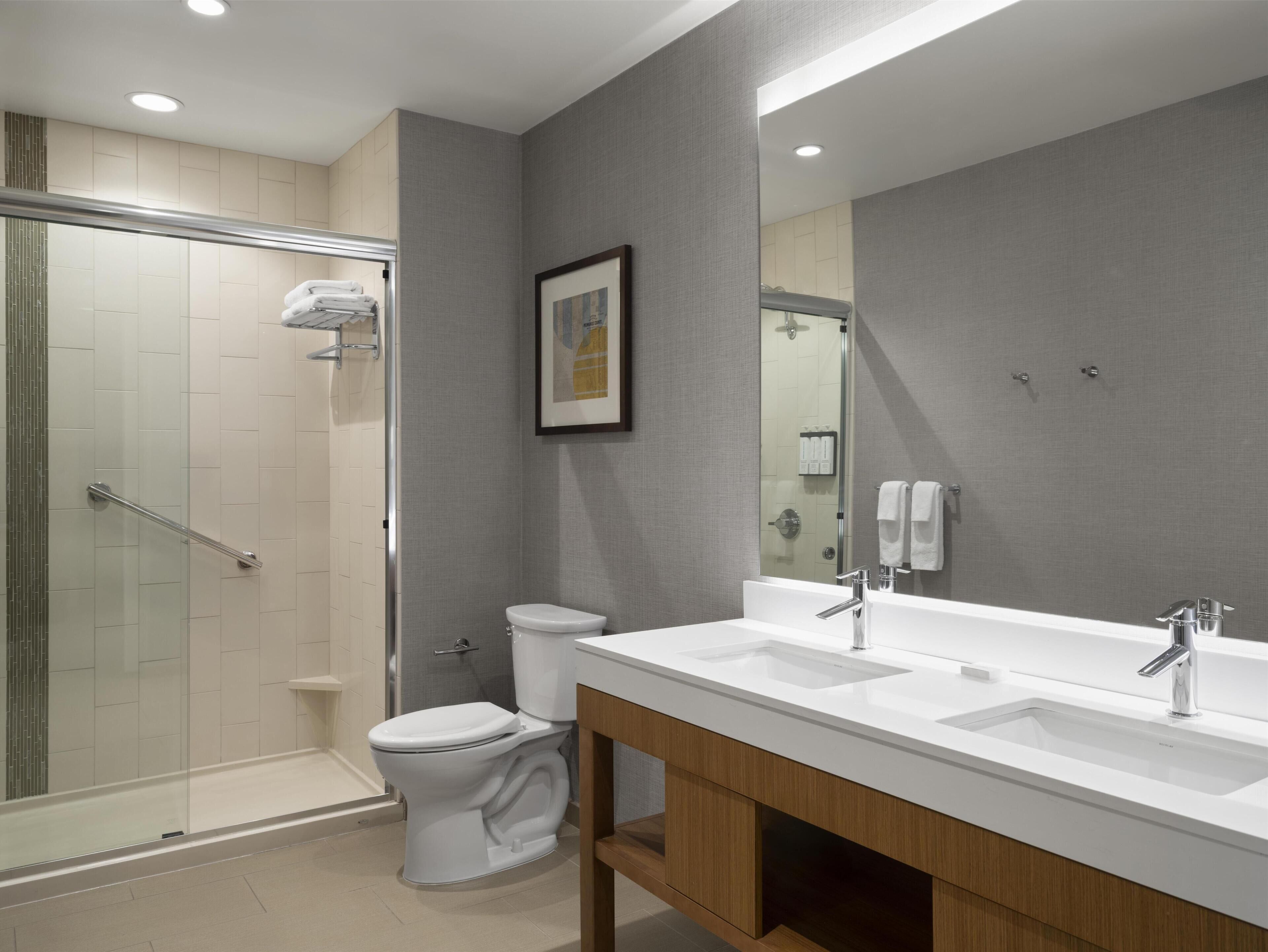 Une salle de bain moderne avec une douche à parois de verre, des toilettes blanches et un meuble-lavabo à deux vasques.