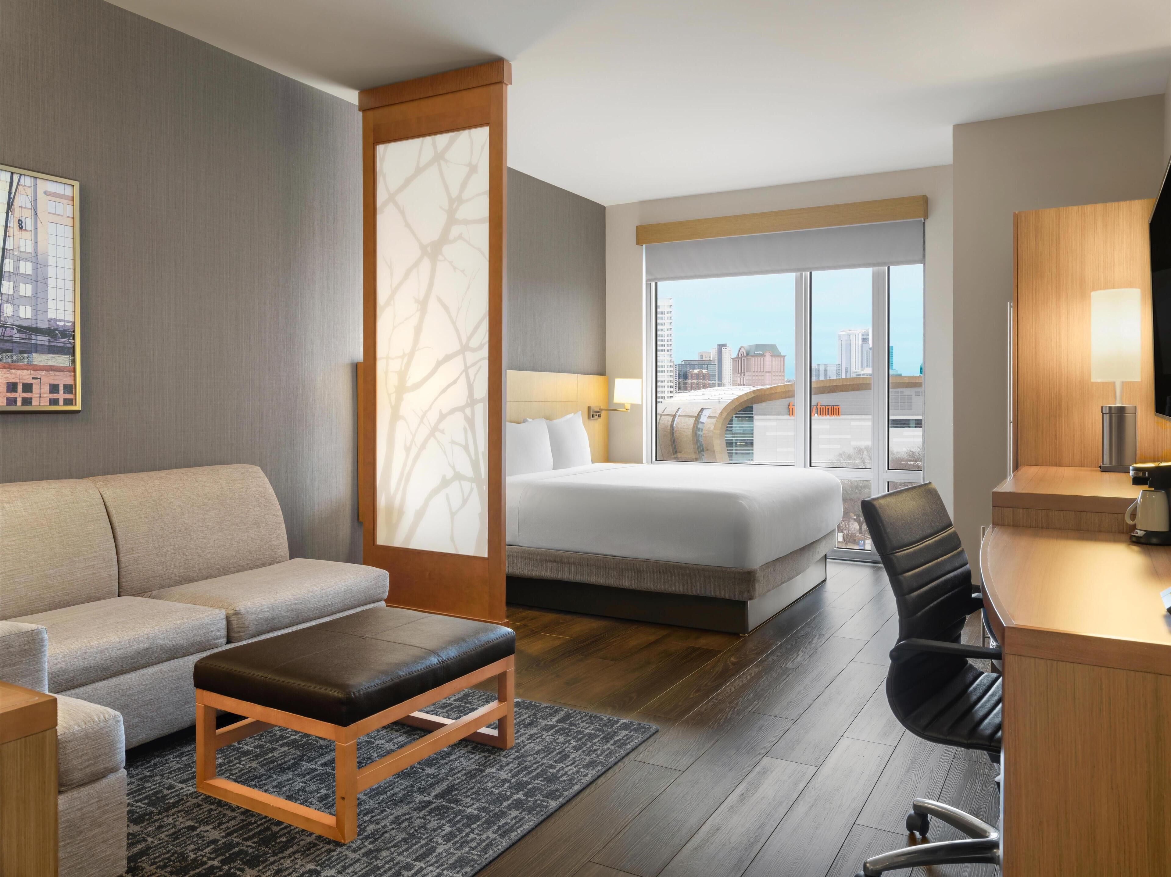 A hotel room with a bed, a sofa, a desk, and a view of the city.