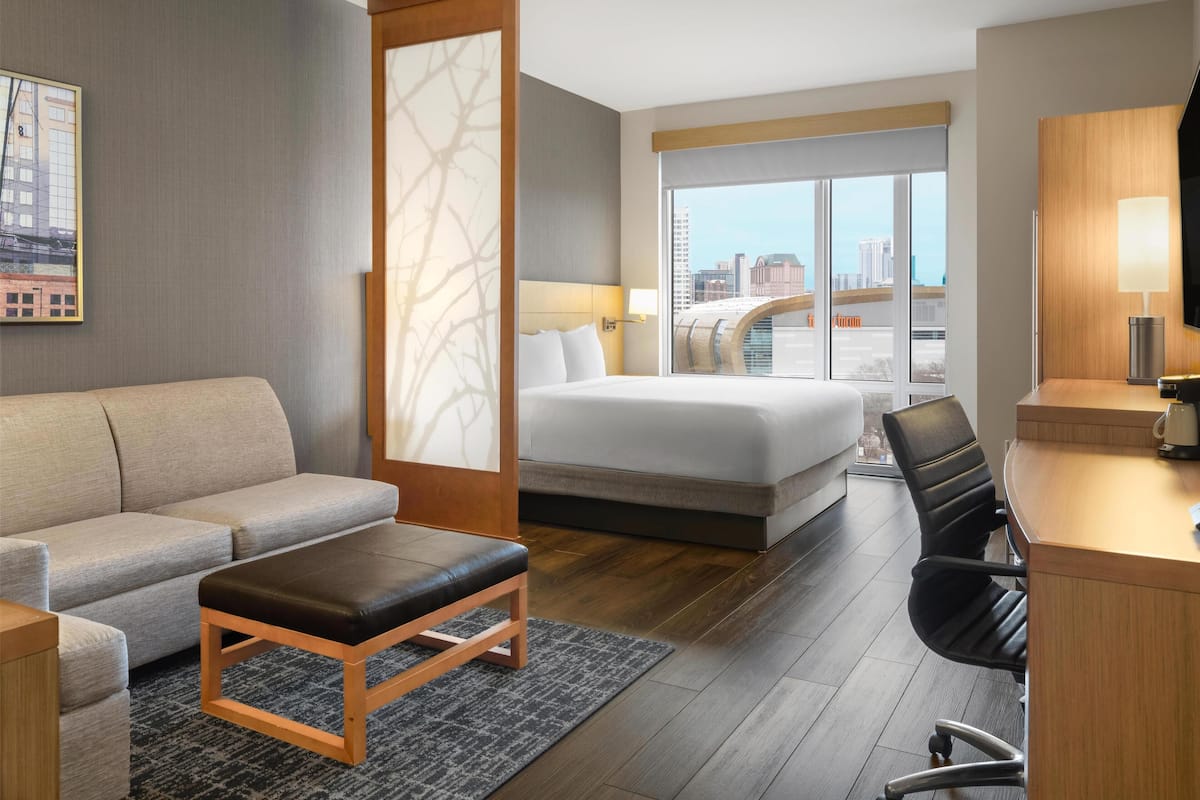 A hotel room with a bed, a sofa, a desk, and a view of the city.