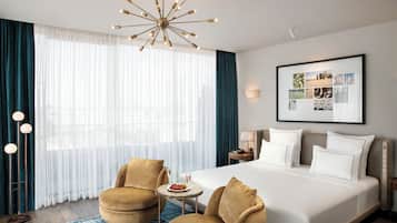 Una camera d'albergo con un letto grande, due poltrone, un tavolino con un piatto di frutta, un lampadario, un quadro appeso alla parete e una lampada da terra.
