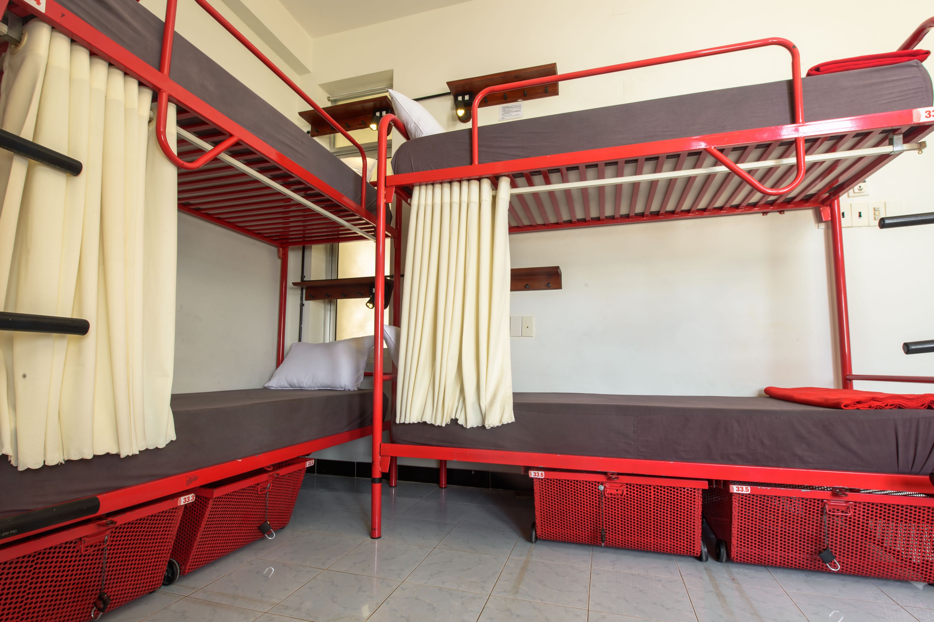 A bunk bed room with red metal frames, white curtains, and a tiled floor.