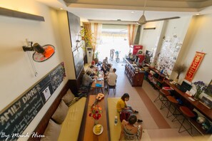 A spacious dining area with high ceilings and a view of the street. There are tables and chairs arranged for dining, and a counter with a Coca-Cola refrigerator.